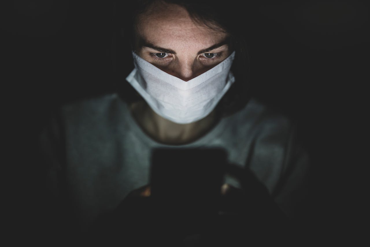 A focused individual wearing a mask uses a smartphone, highlighting the concept of isolation during a pandemic.