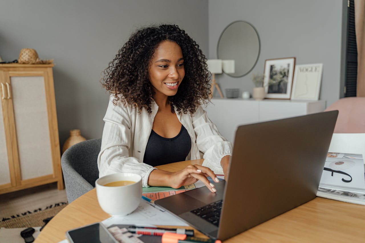 about-02 A woman sits at a round table, working on a laptop with a coffee cup nearby in a cozy home office setting.